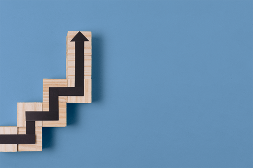 Wooden blocks arranged in a stepped upward pattern with a black arrow zigzagging upward across them against a blue background..